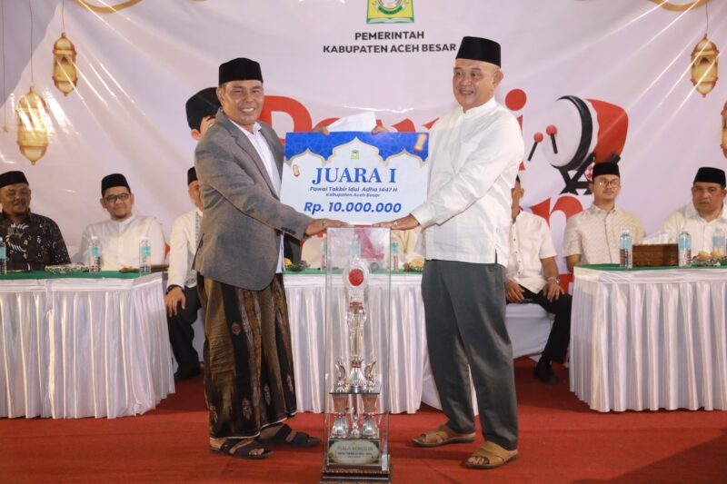 Bupati Aceh Besar H Muharram Idris menyerahkan hadiah pertama kepada Camat Blang Blang Bintang Subhan SE MM sebagai pemenang Pawai Takbiran Idul Adha 1447 H yang digelar Pemkab Aceh Besar di halaman depan Masjid Jamik Lambaro, Kecamatan Ingin Jaya, Selasa malam (26/05/2026).